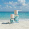 Two bottles of 'Sea Spritz' on a sandy beach with ocean and sky in the background.